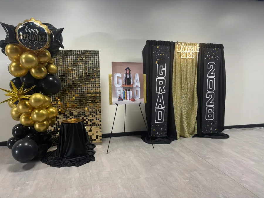 Graduation setup in black and gold: balloon columns, a sequin backdrop and a gold 2026 marquee.