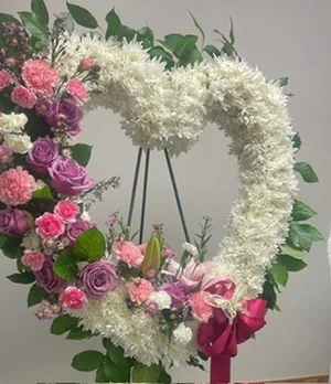 Open-heart wreath of white cushion mums with ivy, on a wire easel, with a pink and lavender flower cluster and fuchsia bow at the base.