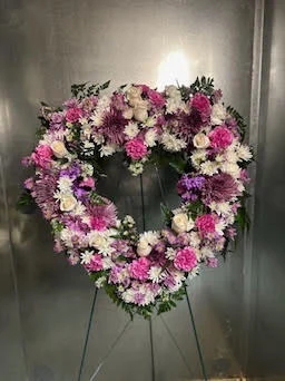 Open-centre heart wreath in purple and white carnations and daisies on a wire easel against the stainless cooler