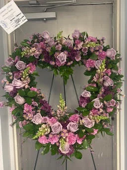 Open-centre heart wreath of lavender and pink roses and stock on a wire easel, card attached, in the cooler