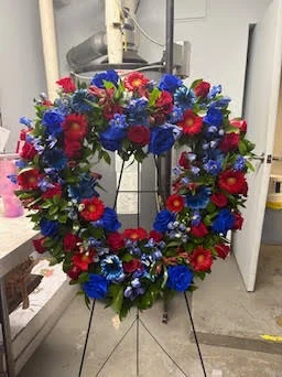 Round wreath in red, white and blue flowers on a wire easel in the workroom — patriotic memorial piece