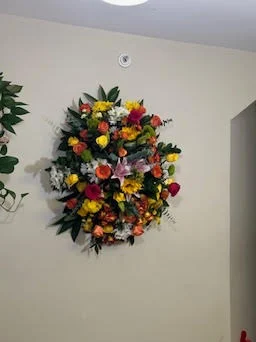 Round wreath of bright yellow, orange and red mixed flowers hanging on a plain white interior wall