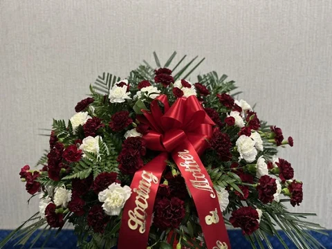 Casket spray of burgundy and white carnations with palm and fern, finished with a red sash lettered Loving Mother.
