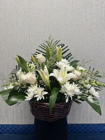 Basket arrangement of white lilies and chrysanthemums with dark greens.